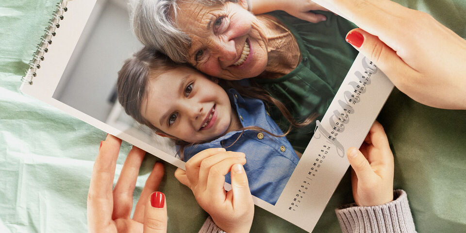 Zwei Personen betrachten gemeinsam einen CEWE Fotokalender mit persönlichen Fotos in der Januaransicht, auf grünem Geschenkpapier.